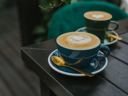 Zwei Kaffeetassen mit Herz-Latte-Art auf einem Tisch, eine in blauer, die andere in grüner Tasse.